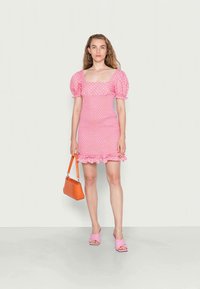 Vestido rosa de mangas bufantes com um decote quadrado, bainha com babados e textura estampada. Combinado com uma pequena carteira laranja e sandálias rosas.