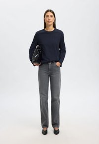 Tumedat pikkade varrukatega särk, hallid sirged teksad, mustad madalad kingad ja must kott ümmarguse sulgemisega. Lihtne disain, minimalism.