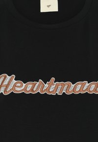 Μαύρο ύφασμα με τη λέξη "Heartmade" κεντημένη σε καφέ χρώμα και περιγράμματος με λευκή κλωστή στη μέση.