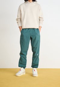 Lehké kalhoty azurové barvy s elastickým pasem, bočními kapsami a bílým logem. Kombinované s béžovou mikinou s kapucí a bílými teniskami.