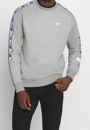 Sweatshirt gris à manches longues, avec un col rond, des poignets côtelés et des accents latéraux ornés d'un motif Nike bleu et d'une marque Nike blanche.
