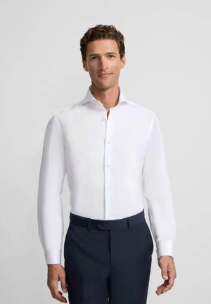 Camisa blanca de botones con mangas largas, cuello recto y textura suave, combinada con pantalones oscuros. Diseño sencillo y limpio sin patrones.