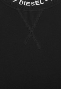 Svart T-shirt med ribbad textur, rund halsringning med vit logotypdetalj och ett X-sticks mönster på framsidan.