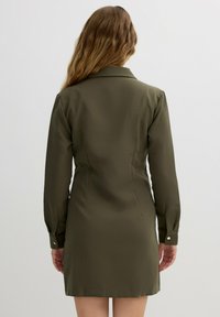 Vestido verde oliva con mangas largas, cuello y puños abotonados. Textura suave con un corte ajustado y un dobladillo corto.