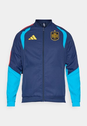 Jūras zilas sporta jaka ar ziliem un sarkaniem akcentiem; tai ir pilna rāvējslēdzēja aizdare, stāvkakls un izšūts ģerbonis. Izgatavota no gludas, vieglas auduma.