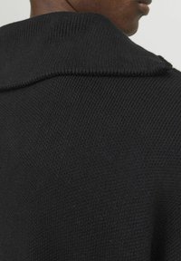 Schwarzer Strickpullover mit strukturiertem Finish, ausgestattet mit einem breiten Kragen und einer engen Passform an den Schultern, die gerippte Details zeigt.