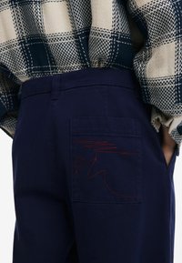 Námornícky bavlnené nohavice so zadnou vreckom s červeným prešívaním. Tkanina má hladkú štruktúru a rovný strih.