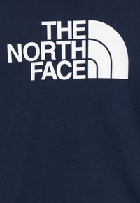 T-shirt bleu marine avec un grand graphique blanc du texte "THE NORTH FACE" accompagné d'un logo courbé. Texture douce, coupe standard, design décontracté.