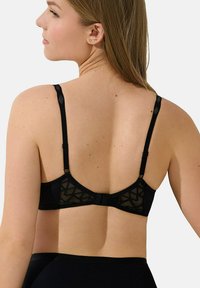 Soutien-gorge noir avec un design en dentelle géométrique, bretelles réglables et fermeture à crochet à l'arrière. Tissu lisse et forme structurée.