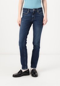 Džínové kalhoty v tmavě modré barvě, slim fit s pěti kapsami. Prošívané detaily na kapsách a pase, v kombinaci s černými mokasíny.