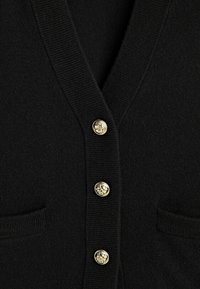 Cardigan noir avec col en V, bords côtelés, boutons décoratifs dorés et deux poches frontales.