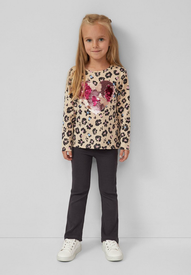 Chemise beige à manches longues avec un motif léopard noir et rose, ornée d'un cœur en sequins. Associée à un pantalon ajusté gris foncé et des baskets blanches.