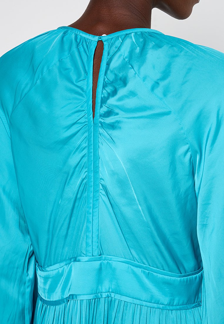Rückenansicht einer Person, die ein leuchtend blaues Satin-Kleid mit hohem Halsausschnitt, einem Schlüsselaugen-Rücken-Detail und einem gerafften Taillennäht trägt.