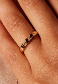 Gouden ring met vijf afwisselend zwarte en heldere stenen, gezet in een gladde band, tentoongesteld op een hand met een gestructureerde huid.