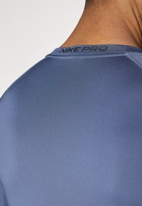Αθλητικό κοντομάνικο πουκάμισο εφαρμοστό στο σώμα σε σ κούρο μπλε χρώμα με απαλή υφή. Διαθέτει λογότυπο «NIKE PRO» στον λαιμό.
