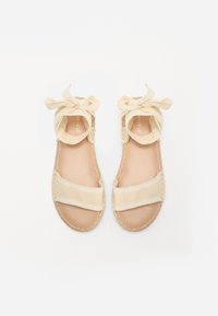 Sandales espadrilles beige avec des liens en tissu, bout ouvert, intérieur doux et semelle en jute cousue, présentant un design minimaliste.