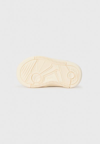 Suela de zapato de goma en un color beige claro con un dibujo de fondo, que presenta un acento circular y líneas texturizadas para un mejor agarre.