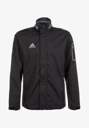 Chaqueta negra de Adidas con cuello alto, bolsillo en el pecho con cremallera y logo en el pecho izquierdo, con ribete reflectante en el bolsillo de la manga izquierda.
