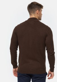 Brauner gestrickter Pullover mit langen Ärmeln und gerippten Bündchen, mit einem Rundhalsausschnitt und einer glatten Textur.