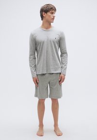 Šedé tričko s dlouhými rukávy a odpovídající kraťasy z měkké látky. Tričko má na hrudi malé logo a kraťasy mají elastický pas.