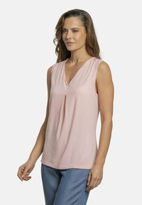 Top sin mangas de color rosa claro con escote en V y sutil detalle de pliegues, hecho de una tela suave. Diseño simple y fluido, adecuado para un uso casual.