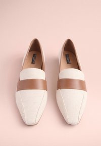 Mocassins à bout pointu en toile beige avec une lanière en cuir marron sur le cou-de-pied. Texture lisse, design discret, esthétique minimaliste.