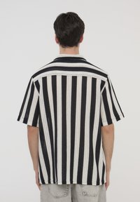 Camicia a maniche corte a righe in bianco e nero, con colletto, vestibilità comoda e tessuto a maglia texturizzato con righe verticali.