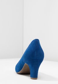 Chaussure élégante en nubuck bleu à talon haut, avec un bout pointu et un talon de taille moyenne, présentant une texture lisse et des détails de couture soignés.