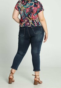 Top de flores colorido de manga corta combinado con jeans ajustados de un azul oscuro y sandalias de tacón marrones, mostrando un diseño detallado y una silueta ajustada.