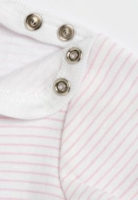 Tissu blanc avec des rayures roses, doté d'un col arrondi et de boutons-pression argentés le long de l'épaule pour une ouverture facile. Texture douce.