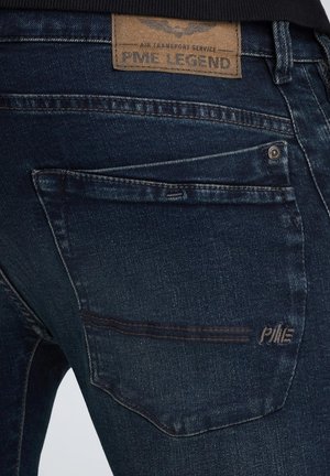 Jeans de mezclilla azul oscuro con una textura suave, que cuentan con una etiqueta de cuero con la inscripción "PME LEGEND" y costuras visibles en el bolsillo trasero.