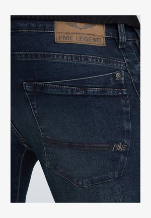 Jeans en denim bleu foncé avec une texture douce, dotés d'une étiquette en cuir portant la mention "PME LEGEND" et d'une couture visible sur la poche arrière.