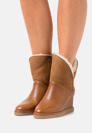 Botas de tobillo de cuña marrones con un forro suave y esponjoso, con un acabado de cuero liso y cierre de cremallera. Parte superior de ante, diseño de punta redonda.