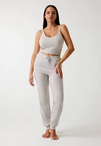 Top corto in maglia grigio chiaro e pantaloni della tuta abbinati. Il top ha spalline sottili e un design aderente; i pantaloni presentano una vita con coulisse e gambe rastremate.