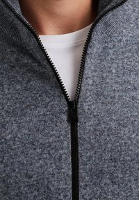 Gray knit zip-up jacket with a high collar, featuring a black zipper and a white crew neck t-shirt underneath. Soft texture, casual design.