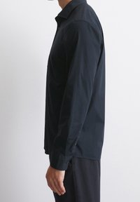 Ciemnoniebieska koszula na guziki z długimi rękawami, kołnierzykiem i subtelnym połyskiem. Posiada mankiety na guziki i prosty krój.