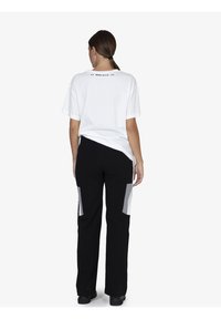 Witte katoenen T-shirt met korte mouwen, zwarte broek met grijze paneelaccenten, getailleerde silhouet, gedragen met zwarte schoenen.