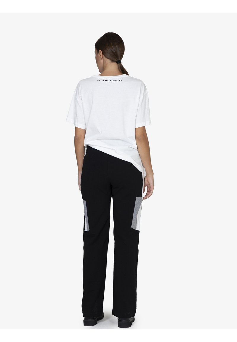 Witte katoenen T-shirt met korte mouwen, zwarte broek met grijze paneelaccenten, getailleerde silhouet, gedragen met zwarte schoenen.
