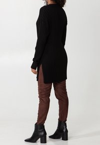 Czarny prążkowany, oversize sweter z bocznymi rozcięciami, zestawiony z brązowymi, wąskimi spodniami z sztucznego zamszu oraz botkami na kostkę z grubym obcasem.