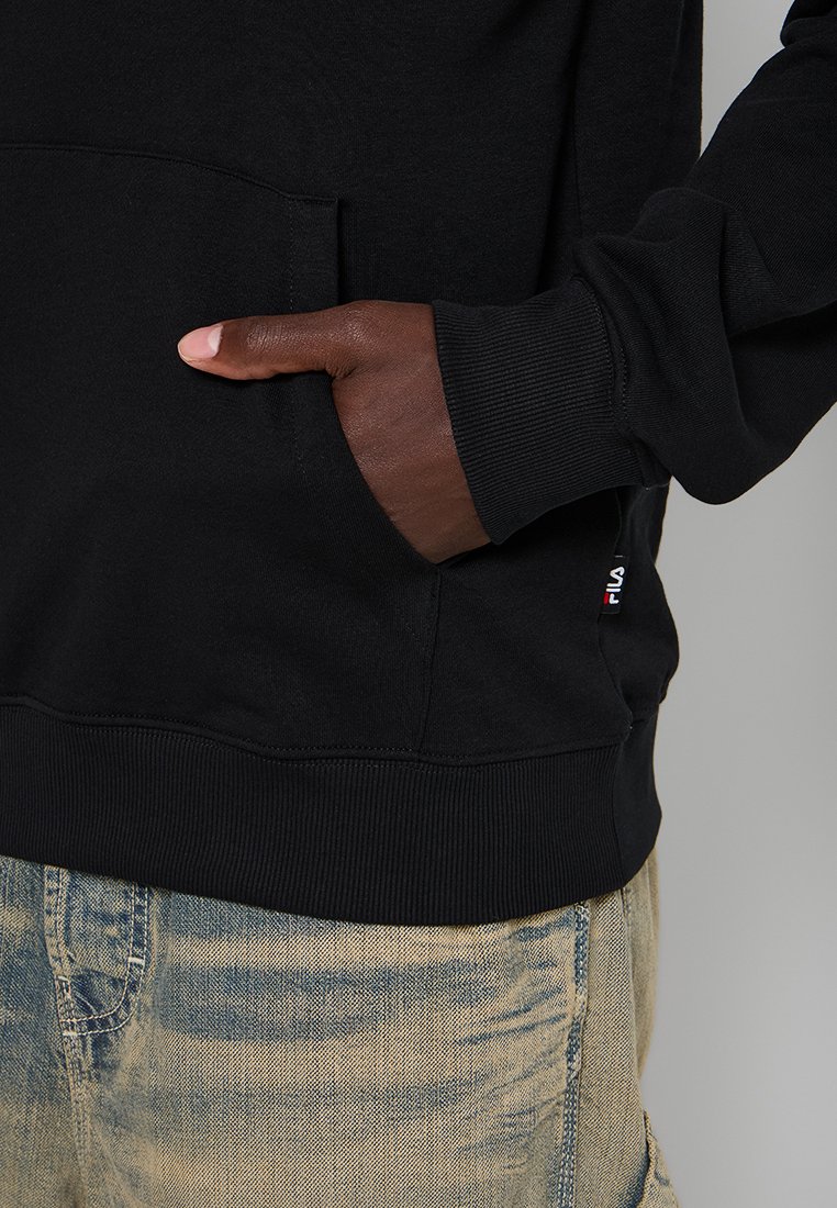 Felpa nera con tasca frontale e polsini a coste, abbinata a pantaloni in denim chiaro, che mette in risalto uno stile casual.