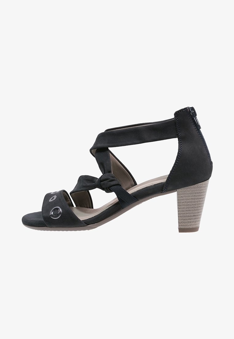 Sandale à talon noire avec un design noué sur le devant, bout ouvert et brides à la cheville. Elle présente des accents circulaires et un talon bloc texturé.