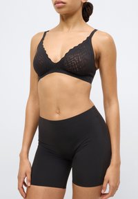 Μαύρο σουτιέν με κυματιστές άκρες και υφασμάτινη υφή, συνδυασμένο με μαύρο σορτς ψηλής μέσης, και τα δύο εφαρμοστά και με λείο φινίρισμα.
