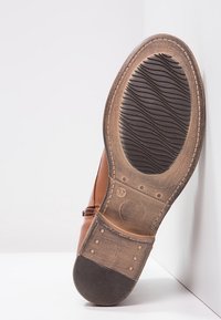 Suela de zapato de cuero marrón con un diseño de goma negra texturizada, costuras visibles y una marca de tamaño (37) en la parte interior.