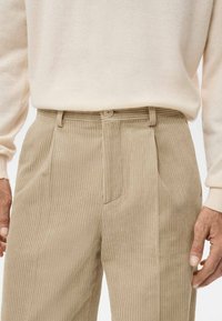 Pantalones beige de pana acanalada con corte recto, con bolsillos laterales y cierre de un solo botón. Tela texturizada y suave.
