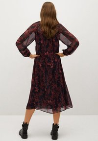 Black floral dress with red plant pattern, featuring sheer long sleeves and a flowy silhouette, paired with black ankle boots.