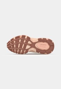 Semelle d'une basket Lacoste rose et marron montrant le motif de la semelle et le logo avec le texte « Lacoste, français pour le meilleur, depuis 1933 »
