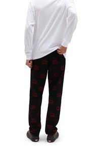 Pantalon de pyjama noir avec des motifs floraux rouges, fabriqué en tissu doux. Porté avec une chemise blanche à manches longues, vue de dos.