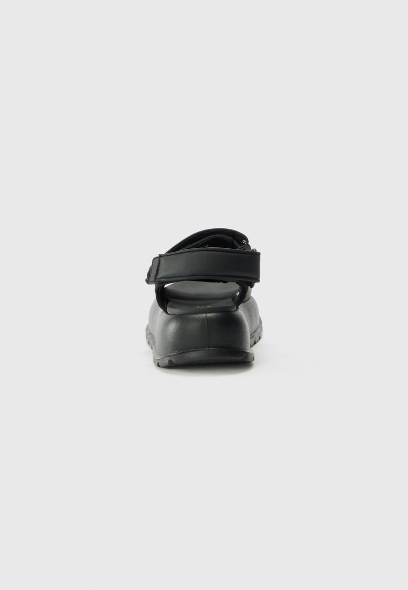 Schwarze Sandale mit einer weichen, matten Oberfläche, verstellbarem Riemen und strukturiertem Gummisohle. Entwickelt für Komfort und einfaches Tragen.