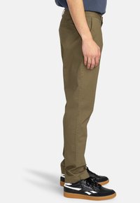 Khaki pants with a straight-leg design, made of cotton, featuring front pockets and a smooth texture. Paired with black sneakers.