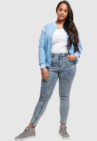 Giubbotto bomber azzurro chiaro con accenti bianchi, t-shirt bianca, jeans in denim sbiaditi a vita alta e sneakers grigie alte.